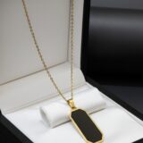 Minimalist golden-tone chain necklace with a black rectangular unisex pendant on a dark background.”