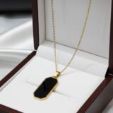 Minimalist golden-tone chain necklace with a black rectangular unisex pendant on a dark background.”